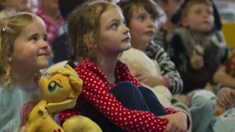 Children sitting down listening, holding teddy bears.
