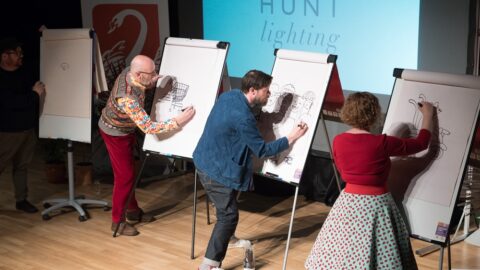 Four people on stage drawing on paper flipboards.